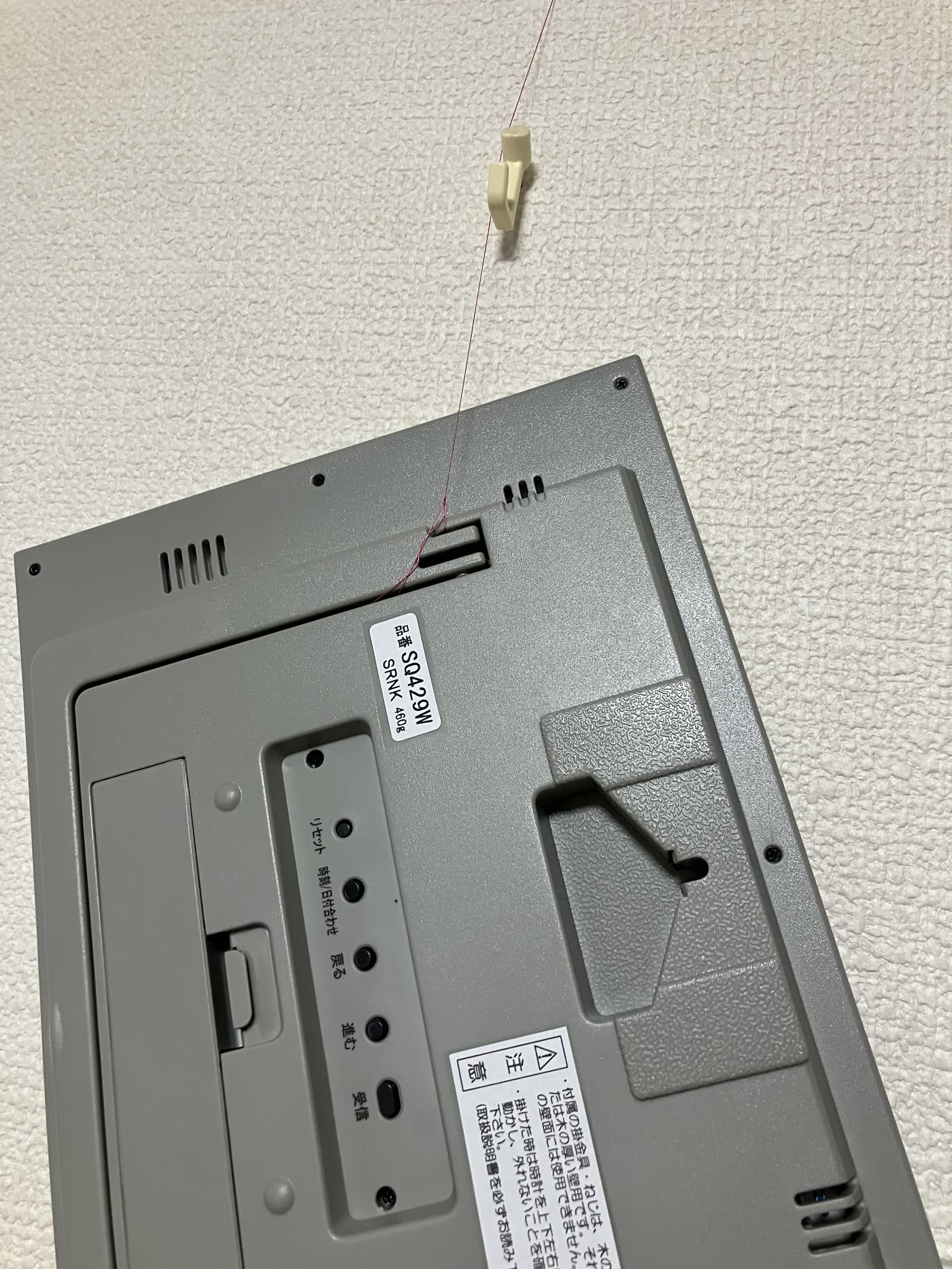 壁掛け時計の裏側に糸を通してピンで止めている例